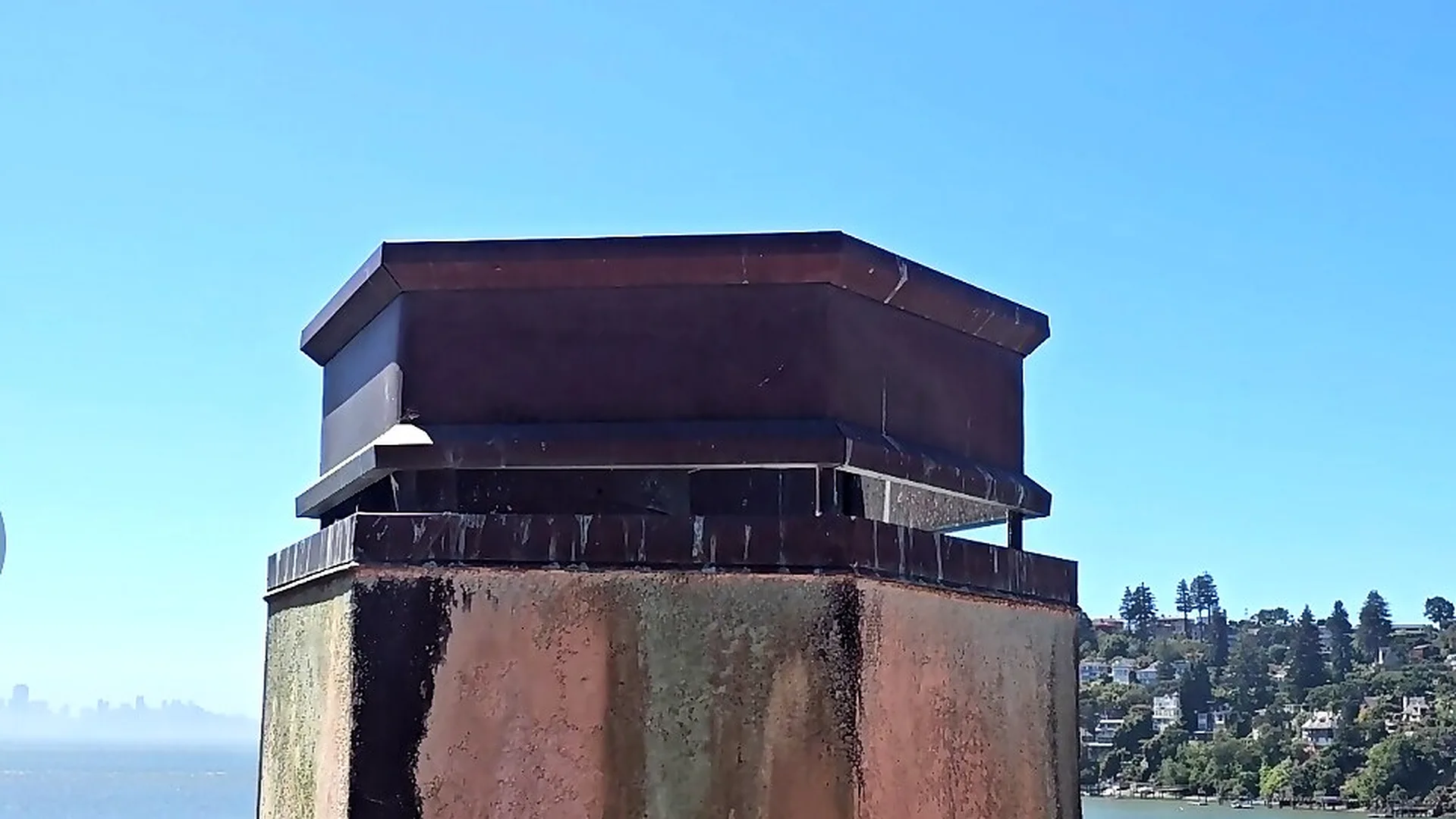 Custom metal chimney cap on a tapered stucco chimney in Marin County with San Francisco Bay behind — Heart's Chimney